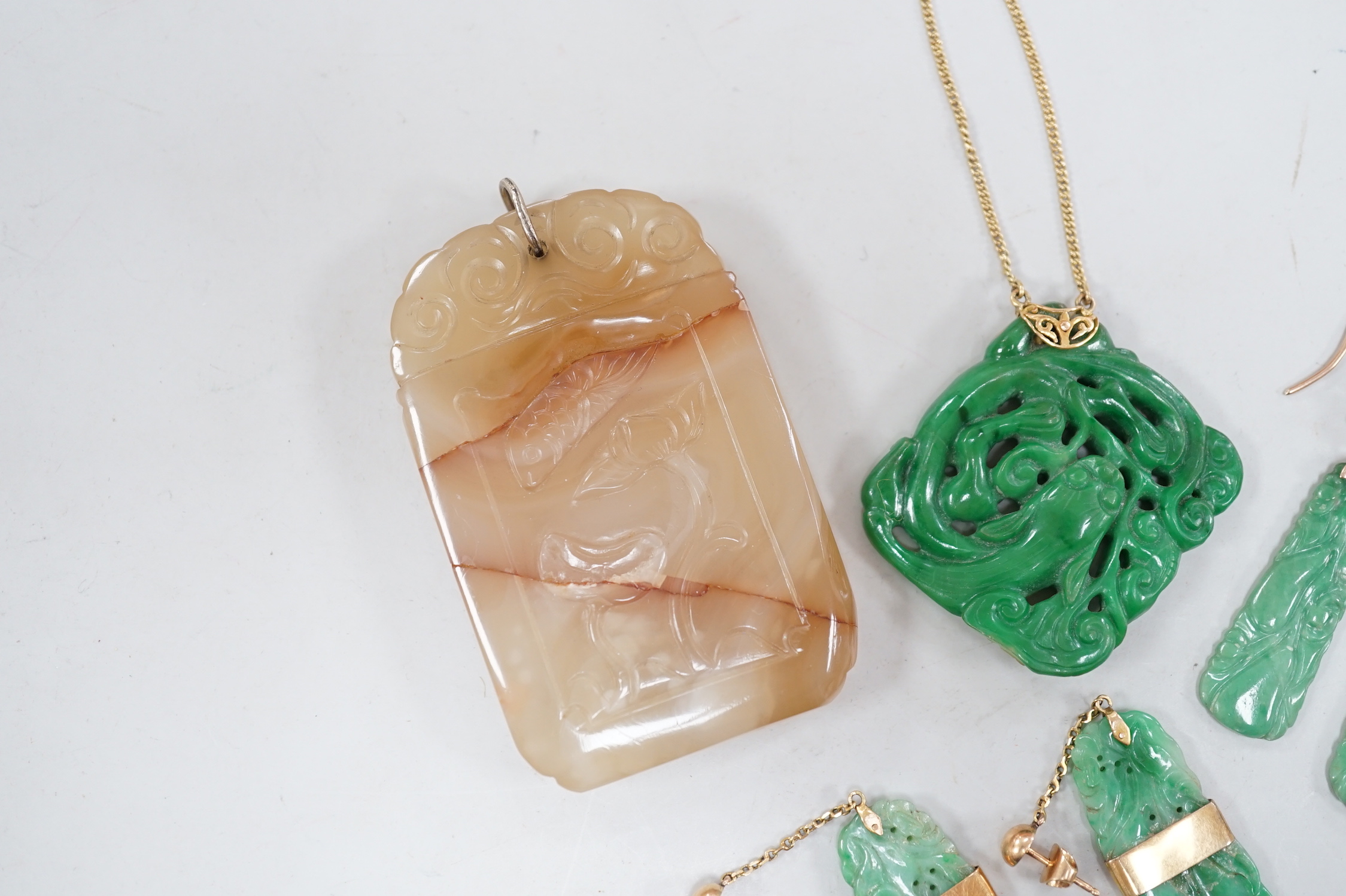 A Chinese carved hardstone pendant, 64mm, a pierced green hardstone pendant on chain and two pairs of yellow metal mounted carved jade earrings.